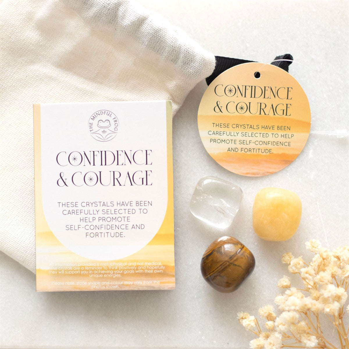 A set of three crystal stones including yellow jasper, clear quartz, and tiger's eye, presented in a drawstring bag with an informative insert card that reads 'Confidence & Courage'.