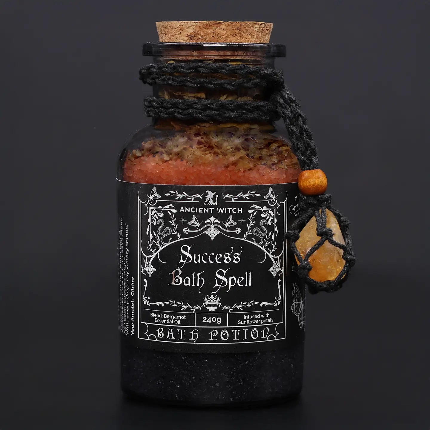 success bath spell glass jar with cork lid and macrame necklace with citrine crystal around the neck of jar on a black background,