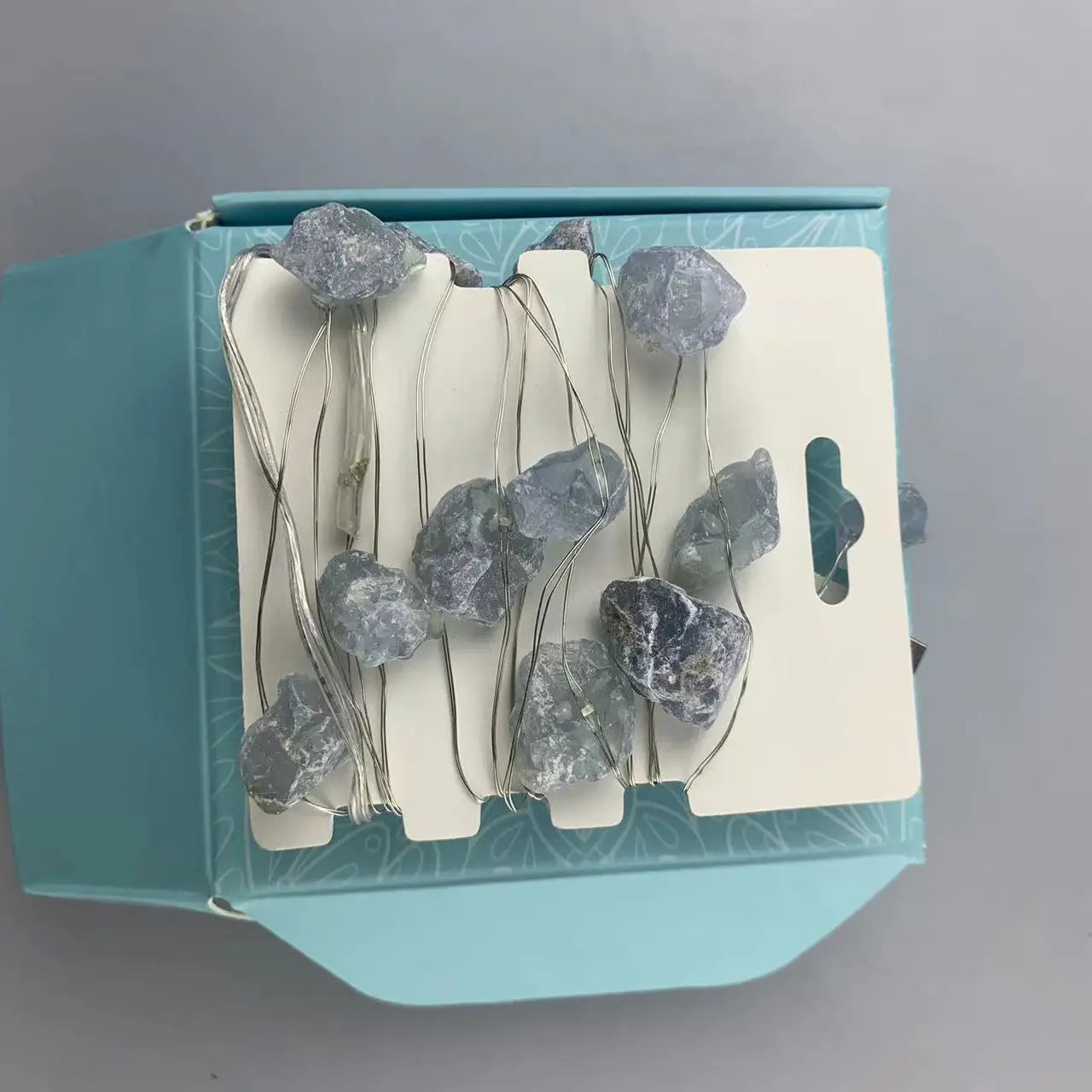 "Celestite Crystal Lights in open ice blue box showing lights on card wrap and USB plug on grey background"