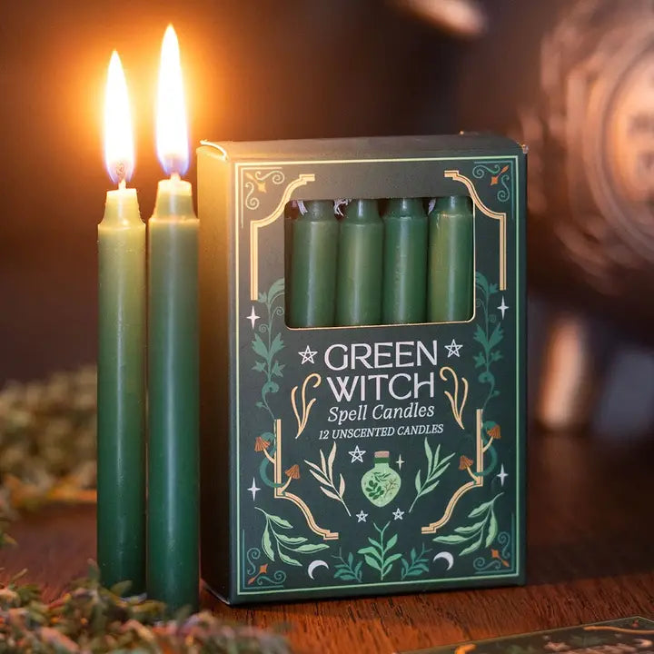 "Green Witch Spell Candles box with lit green candles on wooden table with scattered herbs"